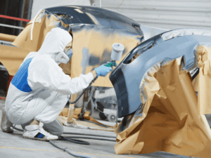 Collision repair spray technician finishing a bumper repaint in Kennewick.